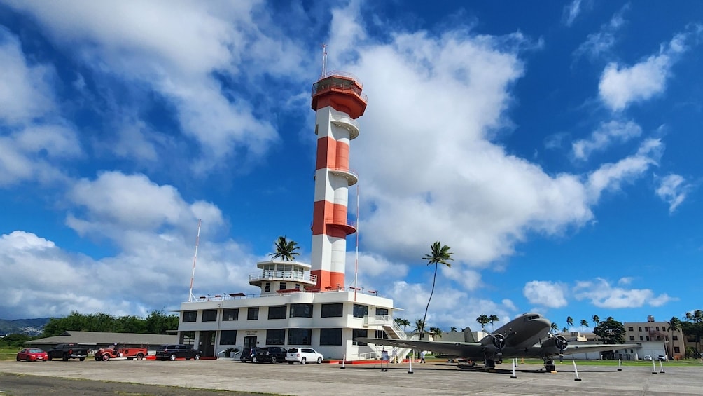 A lighthouse with a red and white striped tower, a control building, and a vintage airplane on display. 3