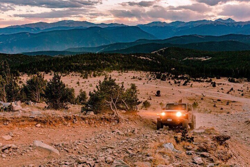 A vehicle driving on a dirt road in a mountainous area with trees and distant mountains. 1
