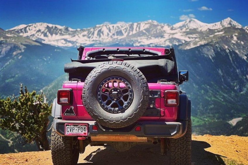 A pink off-road vehicle with a spare tire mounted on the back, parked on a dirt path with a mountainous landscape in the background. 2