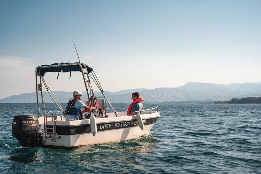 A boat named 'LATCHI WATERSPORTS' on a body of water with mountains in the background. 3