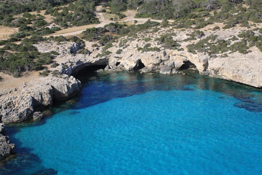 Un paisaje costero con una piscina azul cristalina, formaciones rocosas y vegetación escasa. 2
