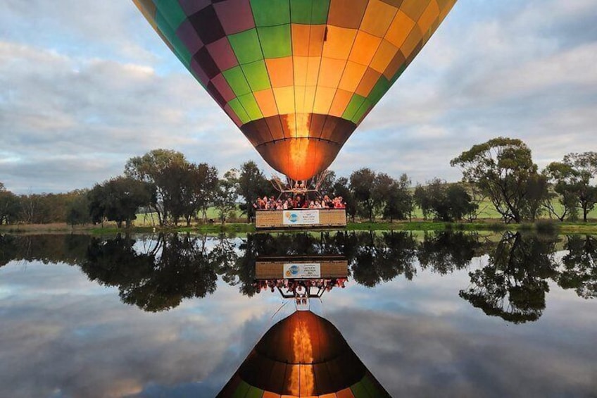 Een luchtballon boven een rustig meer, met een heldere spiegeling, omringd door bomen. 1