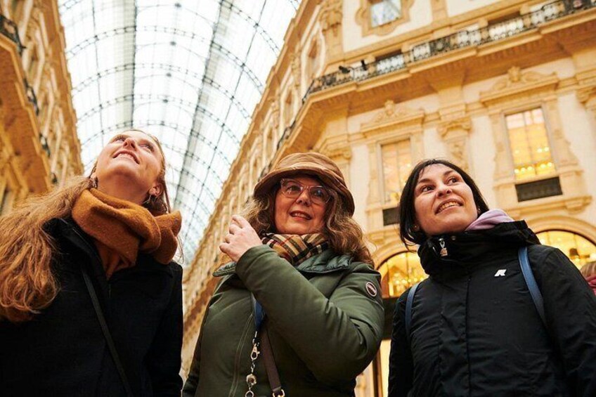 Three people standing in a covered area with a glass ceiling, looking upwards. 2
