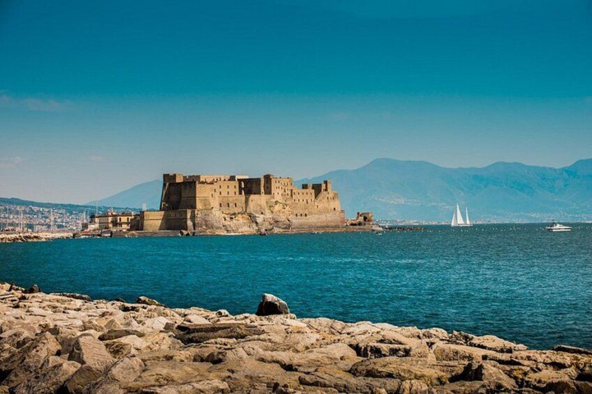 A coastal fortification, rocky shoreline, and sailboats on the water. 1