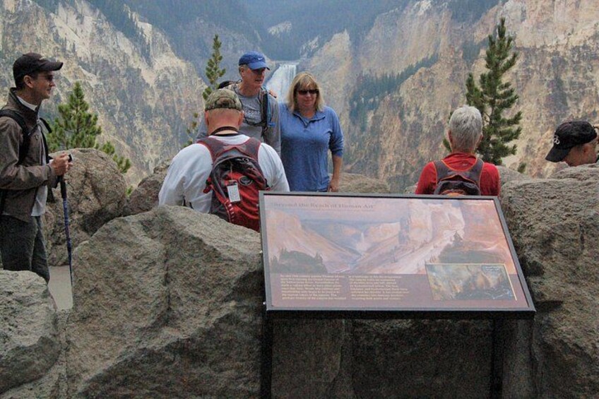 A group of hikers at a mountain viewpoint with a large informational sign. 4