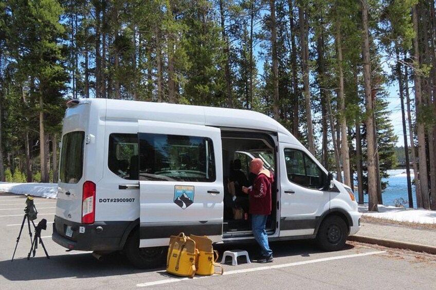 A white van parked on a road with a person standing next to it, a tripod, and a yellow bag. 2