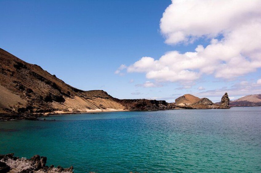 A coastal landscape with clear turquoise waters, rocky hills, and a prominent rock formation. 2