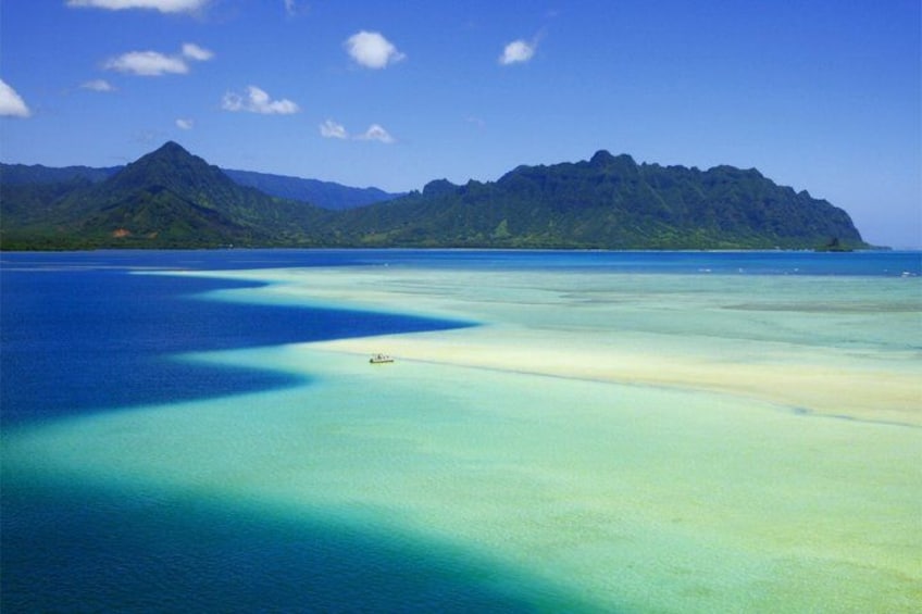A turquoise sea with a boat, a sandy beach, and a mountain range in the distance. 1