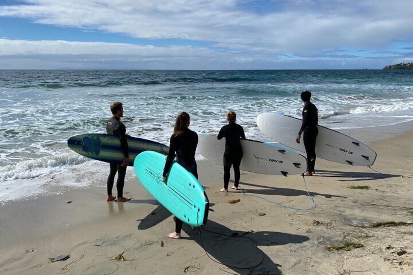 Quatre personnes sur une plage, tenant des planches de surf, avec des vagues en arrière-plan. 4