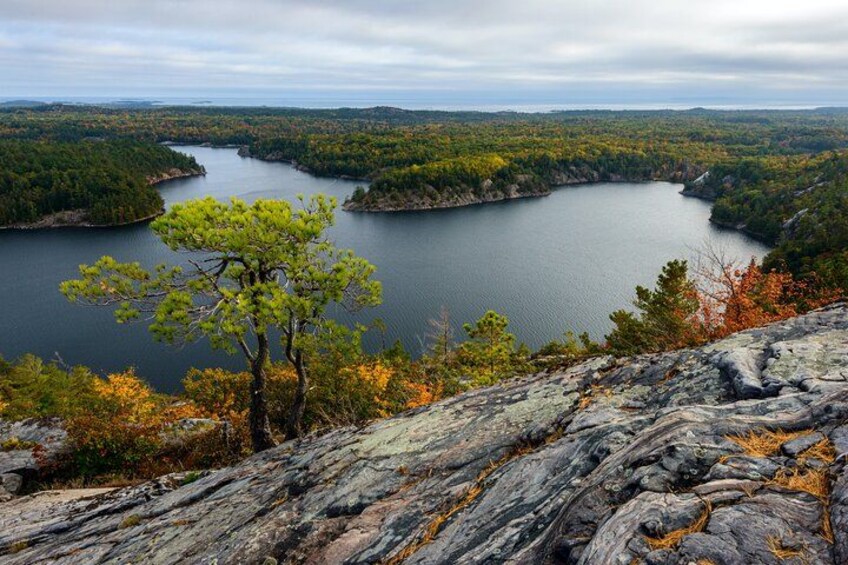 A lake surrounded by forested hills, a prominent rocky outcrop in the foreground, and a clear sky. 3