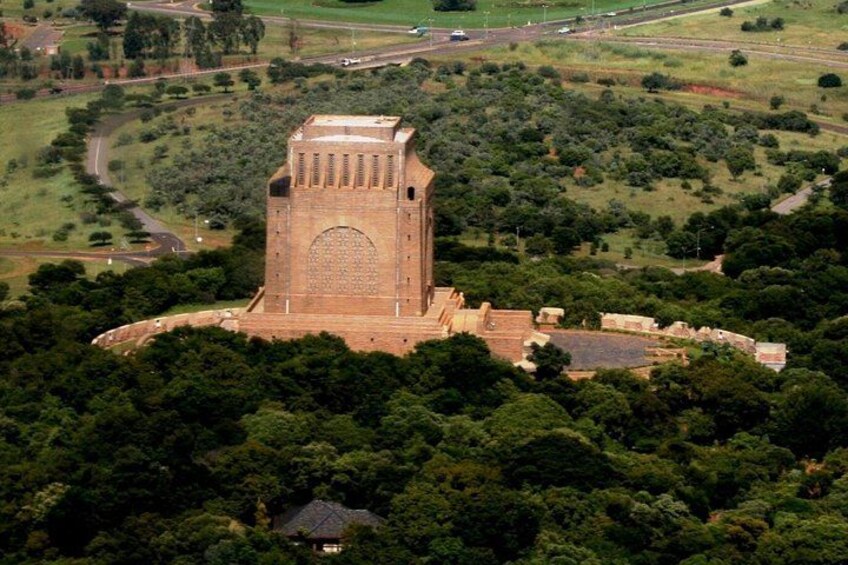 A large, historic stone tower surrounded by dense green forest and a winding road. 1