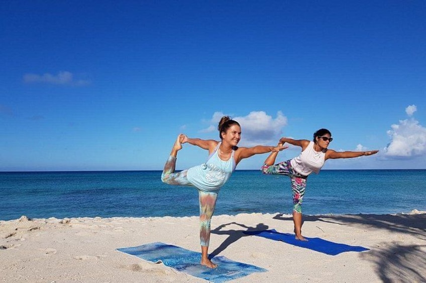 Två personer utövar yoga på en strand med en klarblå himmel och havet som bakgrund. 1