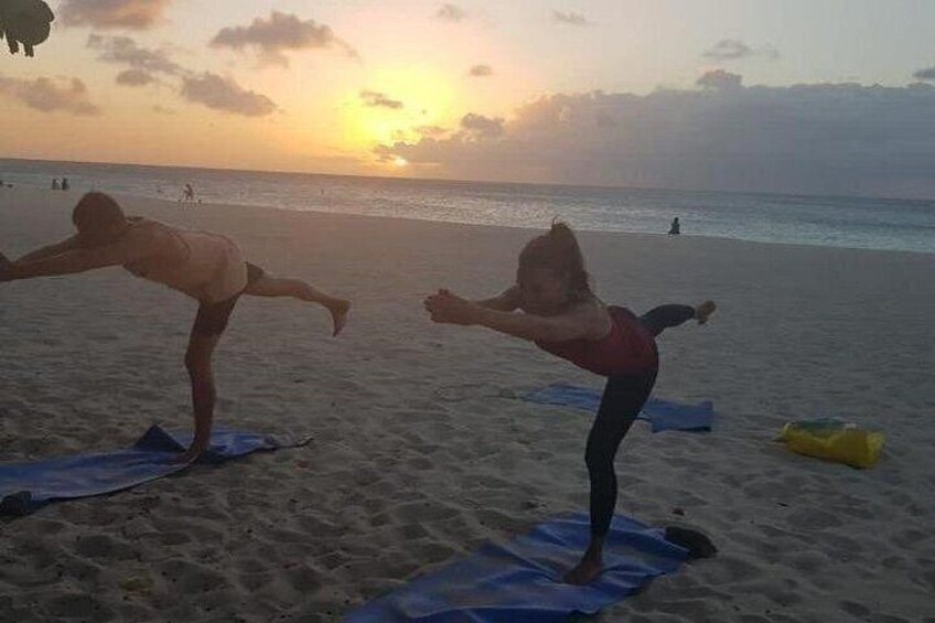 Två personer utövar yoga på en strand vid solnedgången. 5