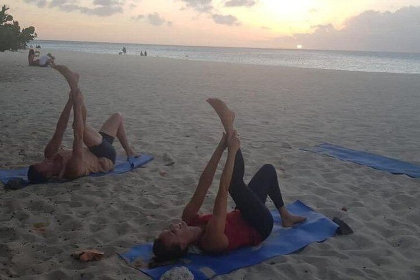 Två personer gör situps på blåa mattor på en sandstrand med havet i bakgrunden. 4