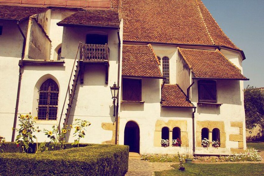 Un bâtiment historique doté d’un toit recouvert de tuiles, de fenêtres en arc de cercle et d’un jardin bien entretenu. 3
