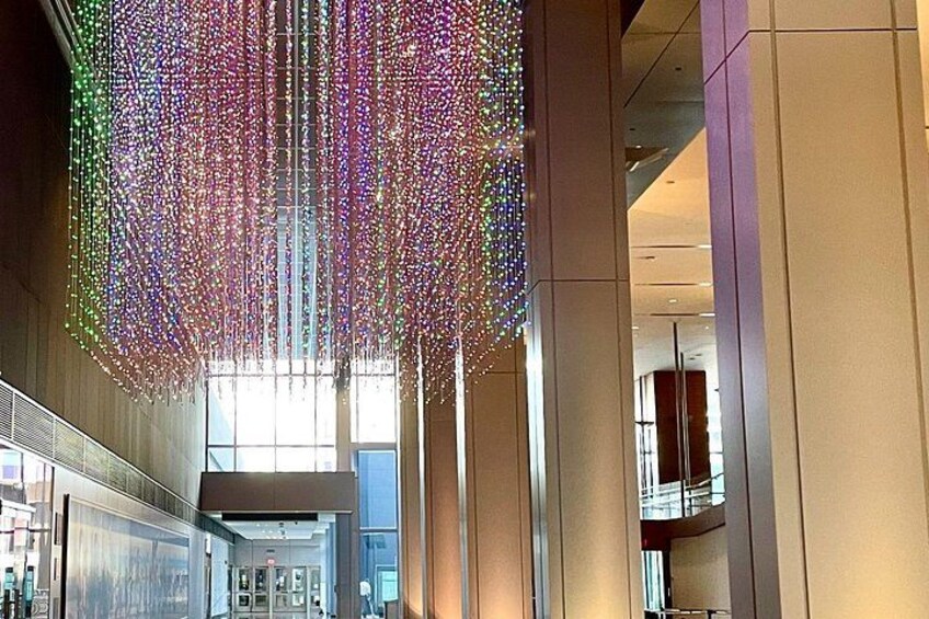 En modern byggnadsinteriör med en stor, färgstark hängande ljusinstallation. 2