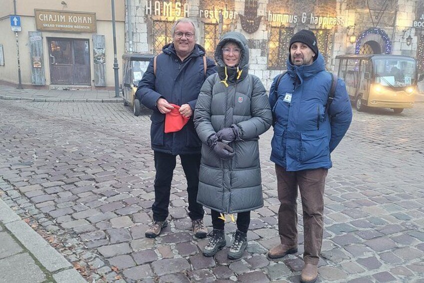 Tre personer står på en brostensbelagt gade med butikker i baggrunden. 3
