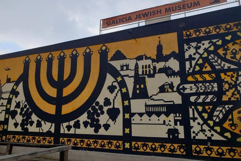 A mural with a menorah, buildings, and a sign for the Galicia Jewish Museum. 4