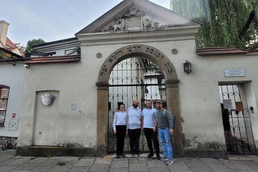 A group of people standing in front of a building with a large arched entrance and a sign with Hebrew text. 5