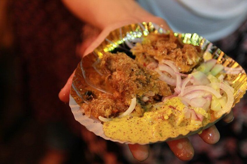 A person holding a foil plate with food, including fried items and a yellow sauce. 2