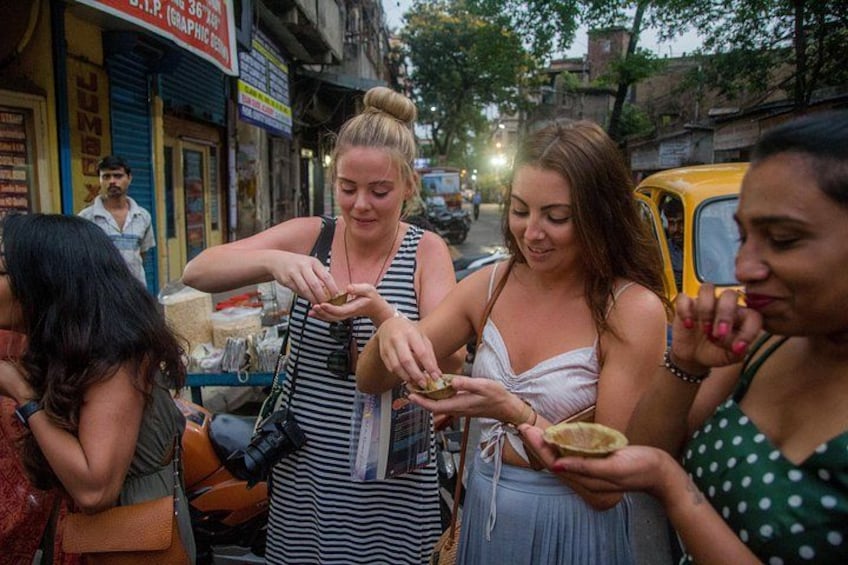 A street scene with people eating street food, a yellow auto-rickshaw, and shops with signs. 2