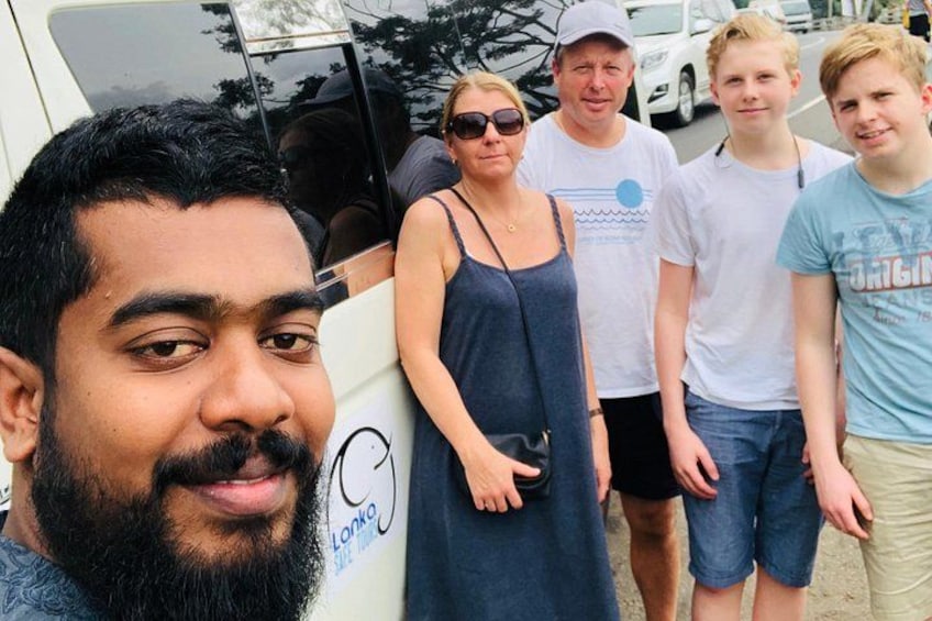 A group of people standing in front of a white vehicle with a surfboard. 4