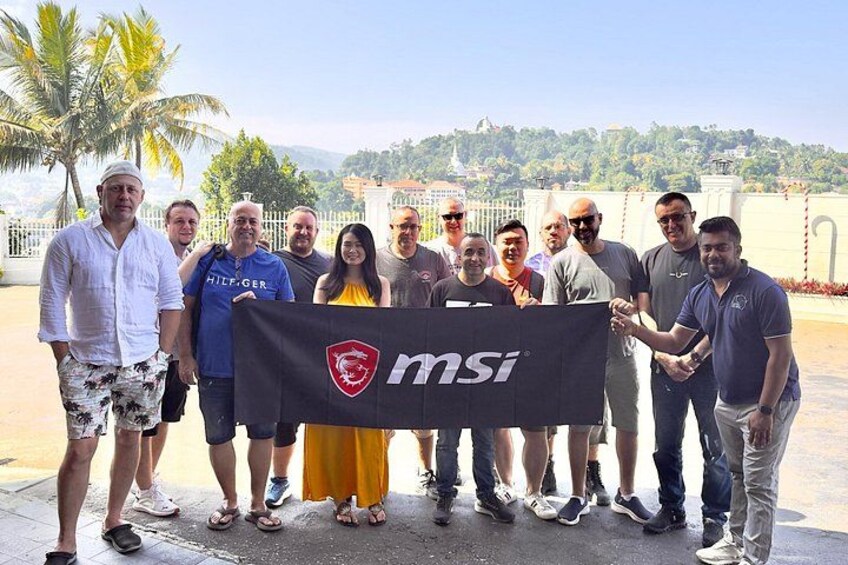 A group of people holding a banner with the MSI logo, standing outdoors with palm trees and a building in the background. 3