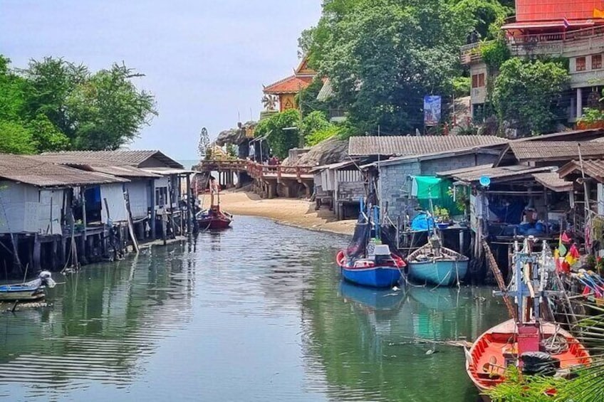 A riverside village with boats docked along the water, traditional houses, and a temple in the background. 1
