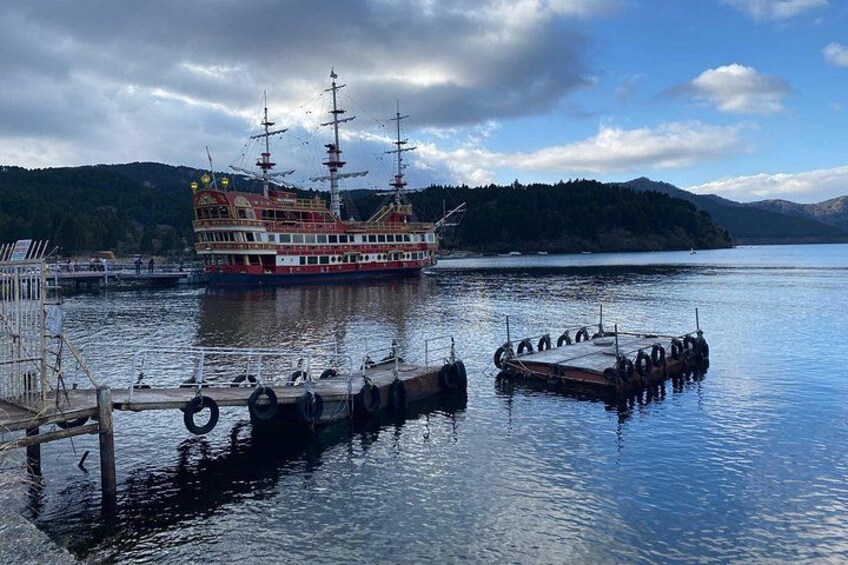 A large, multi-decked ship docked at a pier with a forested island in the background. 1