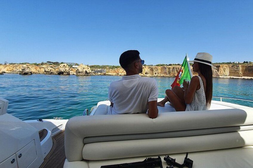 A boat with two people, one holding a flag, and rocky cliffs in the background. 2