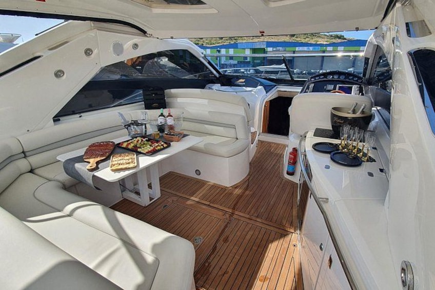 A yacht interior with a dining area, seating, and a small kitchen setup. 4