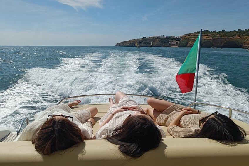 A boat with two people reclining on the deck, a flag, and a coastline in the background. 3