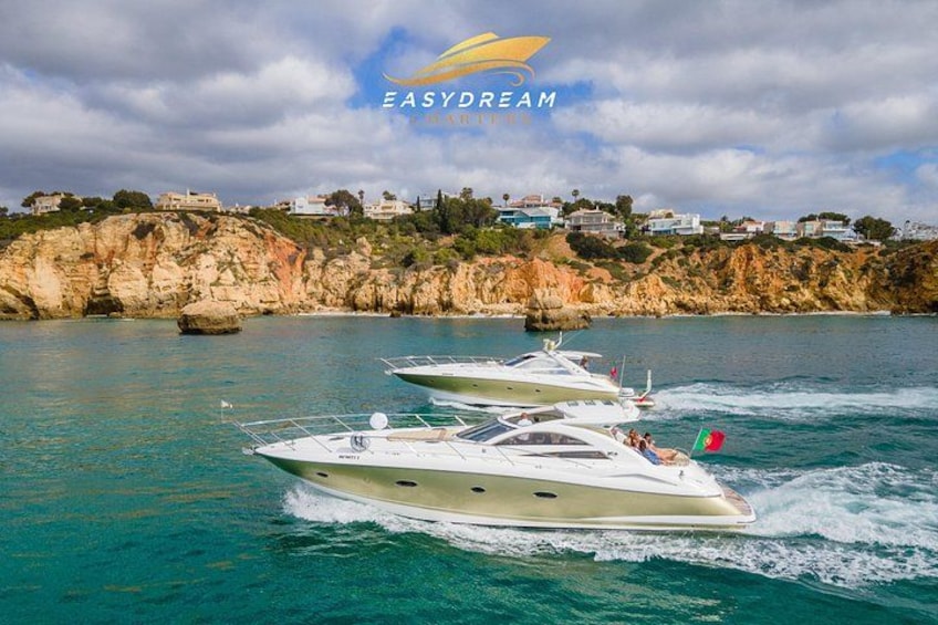 Three yachts on a calm sea with a rocky coastline and houses in the background. 1