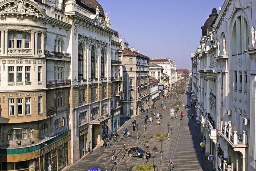 A wide street lined with historic buildings, a clear sky, and a few pedestrians. 1