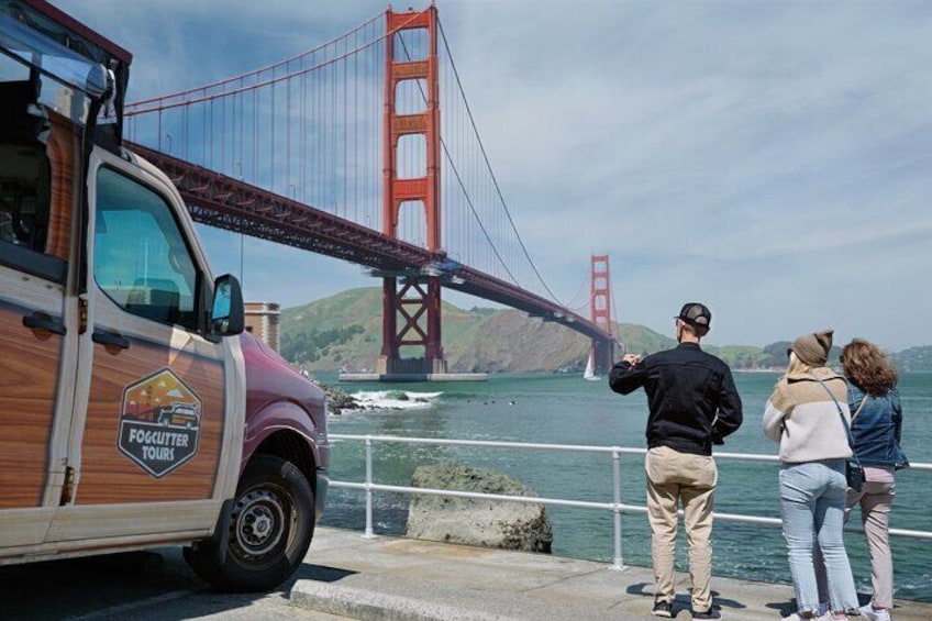 A tour bus with 'Foghopper Tours' logo parked by the Golden Gate Bridge. 1