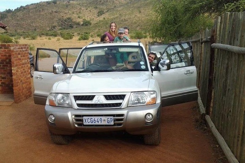A silver Mitsubishi pickup truck parked on a dirt road with a brick wall and wooden fence in the background. 2