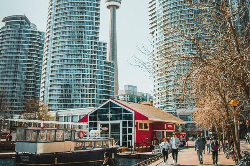A waterfront area with a red building, a boat docked nearby, and tall modern buildings in the background. 5