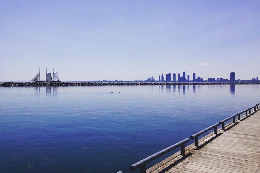 A calm waterfront with a wooden pier, sailboats, and a city skyline in the distance. 4