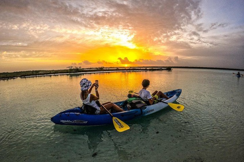 Due persone in un kayak blu su acque calme, con un tramonto sullo sfondo. 1