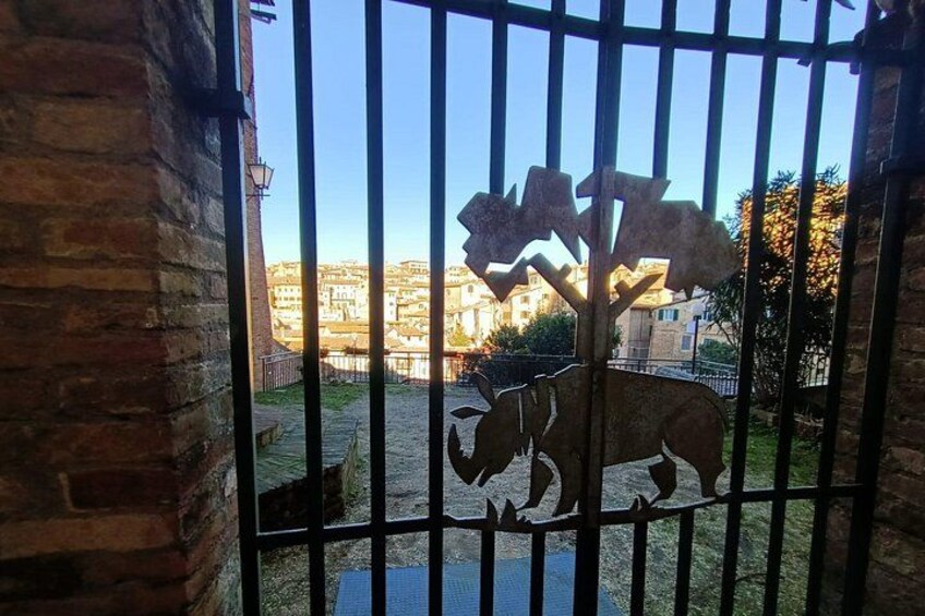 A metal gate with a rhino silhouette, brick walls, and a view of a cityscape in the background. 5