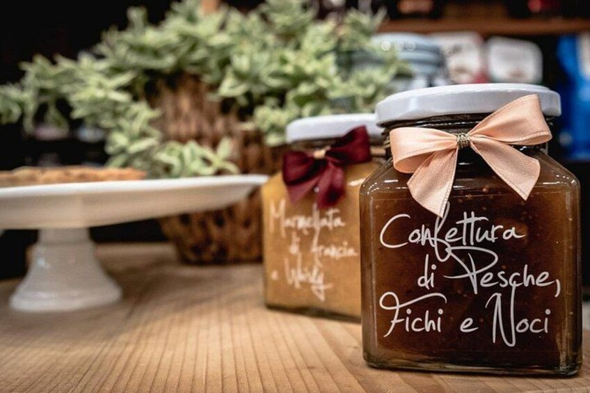 Two glass jars with labels and ribbons, placed on a wooden surface with a white cake stand and green plants in the background. 2