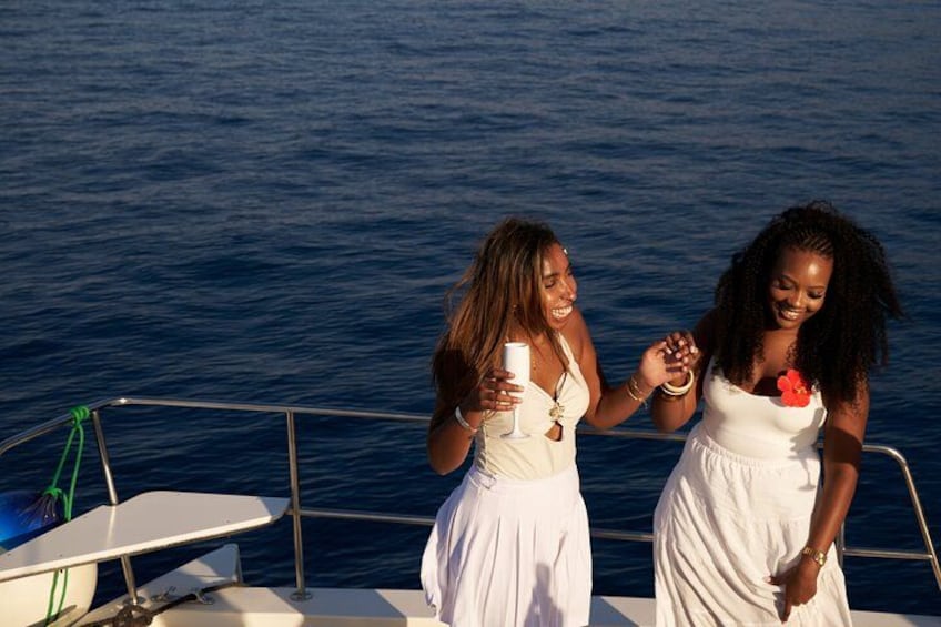 Two women in white dresses on a boat, holding hands and smiling. 4