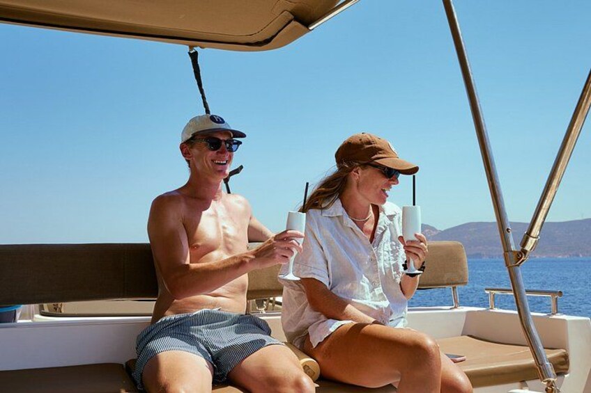 Two people on a boat, one holding a drink, with a clear sky and water in the background. 2