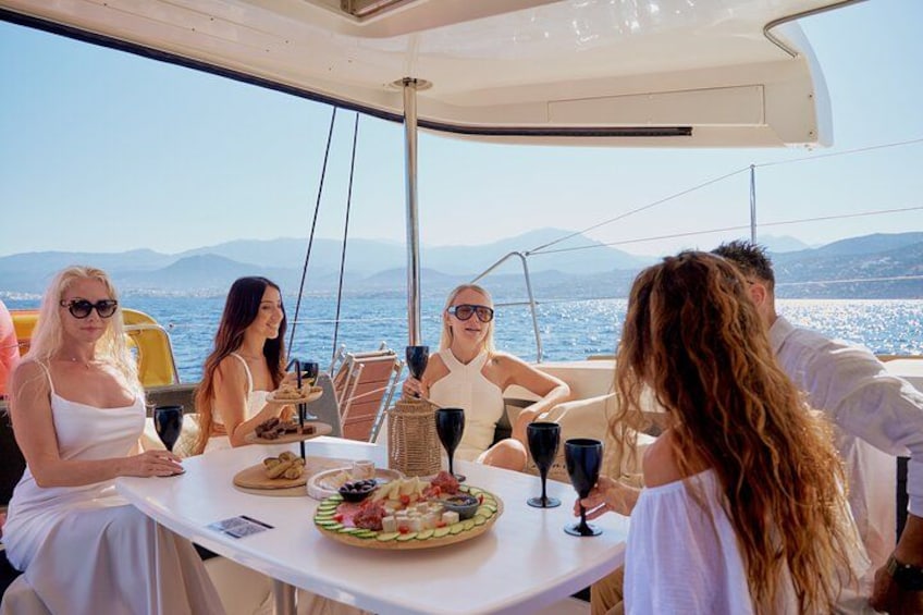A group of people on a boat with a table set for a meal, a clear view of the sea and mountains in the background. 4