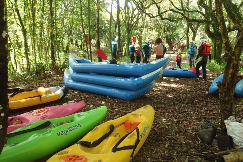 A forest with several kayaks and rafts, some with people wearing life jackets. 3