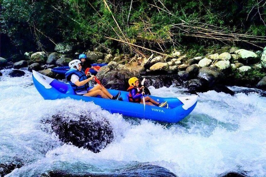 A blue raft with two people navigating a river rapids. 1