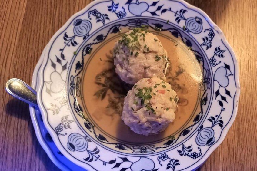 Une assiette décorative ornée de motifs floraux, sur laquelle reposent deux boulettes de viande nappées d’une sauce crémeuse et garnies d’herbes fraîches. 3