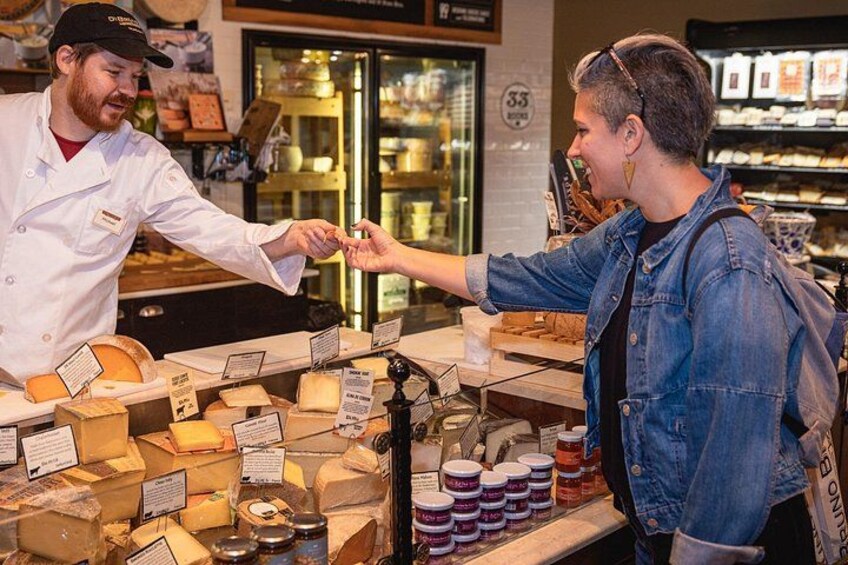 A cheese shop with various cheeses on display and a customer interacting with a shopkeeper. 3
