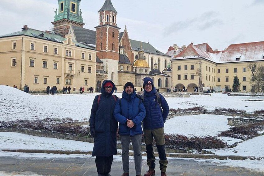Tre personer står på en snötäckt innergård med historiska byggnader i bakgrunden. 3