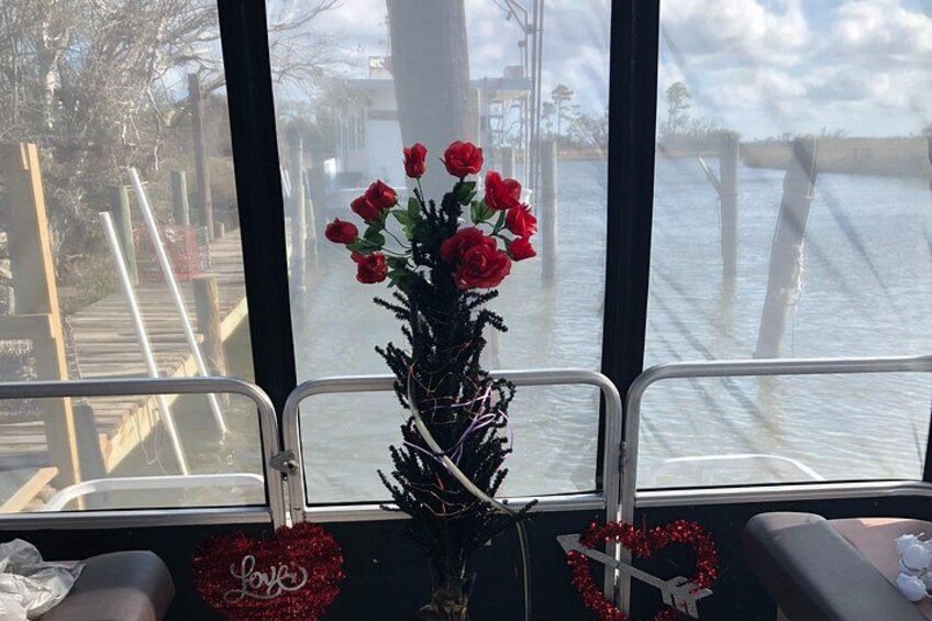 Una ventana con un jarrón de flores rojas, un adorno con forma de corazón y vista a un muelle y al agua. 2